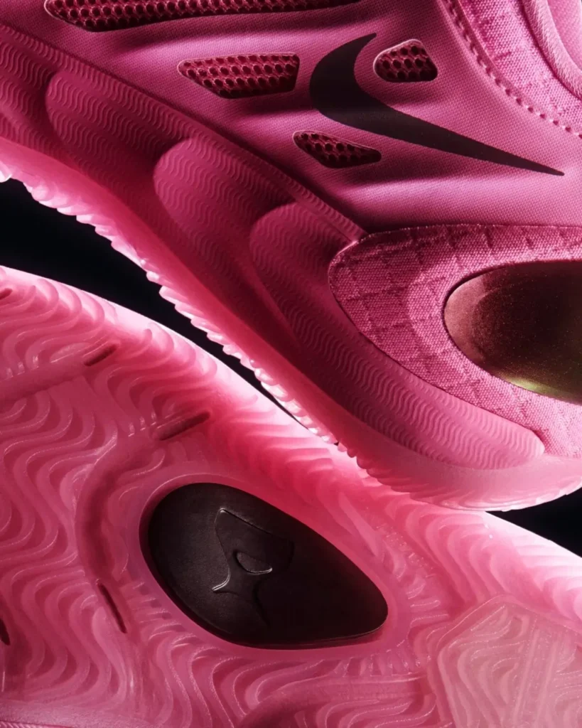 Close-up of the Nike A’Two in bright pink, highlighting the sculpted foam midsole, breathable mesh ventilation panels, black Swoosh logo, iridescent heel counter, and translucent outsole with wavy multidirectional traction pattern and A’ja Wilson logo detail