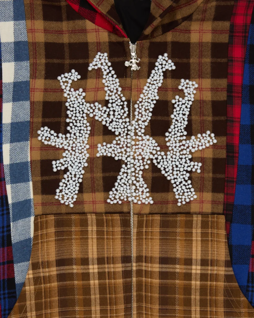 Close-up of Stolen Arts Flannel NY Pearl Hoodie featuring pearl-studded NY logo on brown plaid patchwork with zip front and mixed flannel panels