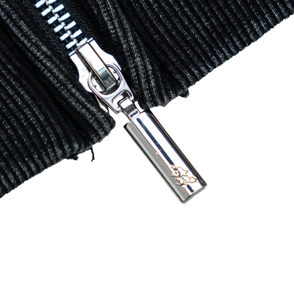 Close-up detail of the Free Refills Amoeba Zip-Up Hoodie zipper showing a polished silver metal zipper pull with engraved star graphics against washed black ribbed cotton fabric