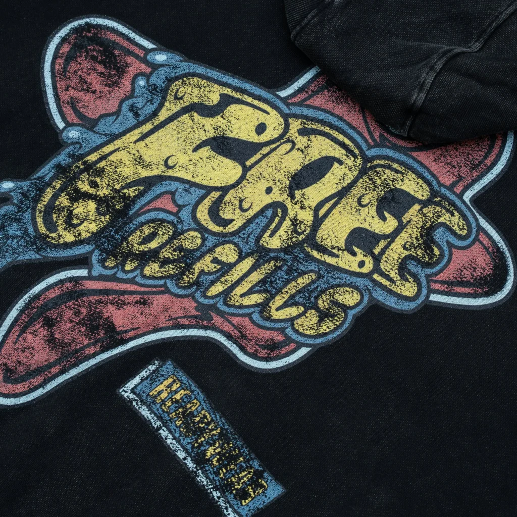 Close-up of the Free Refills Amoeba Zip-Up Hoodie back graphic showing distressed yellow “Free Refills” lettering layered over a pink amoeba-shaped background with blue outline on washed black fabric