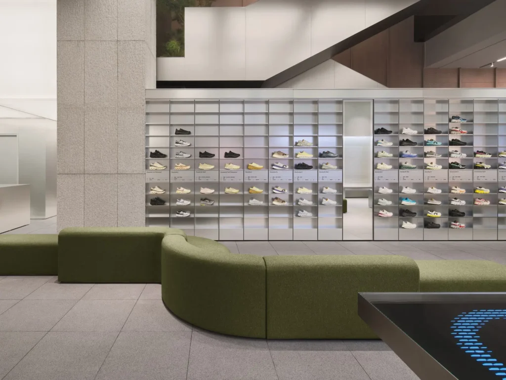 Wall display of performance sneakers inside the On Running flagship store at MixC World with modular shelving, curved green seating, and minimalist Swiss-inspired retail architecture