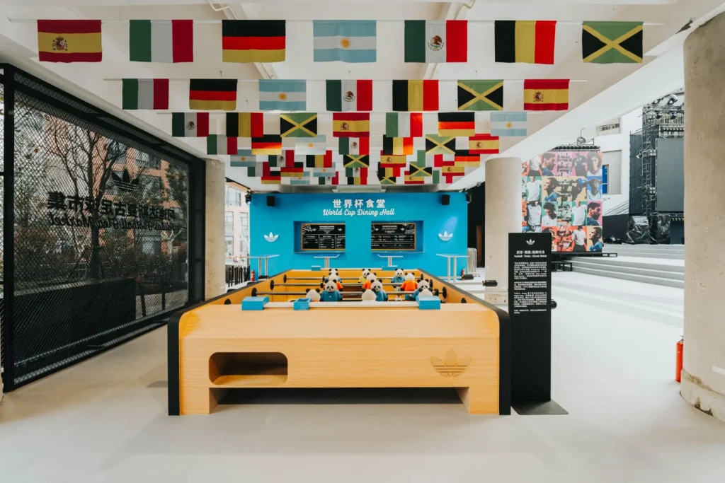 adidas World Cup Dining Hall activation featuring a foosball table beneath a ceiling of international flags inside Shanghai football flea market experience