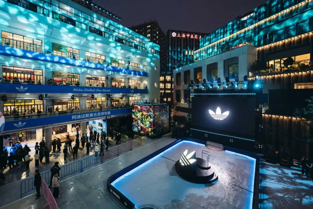 Immersive adidas football flea market stage in Shanghai featuring a glowing mini pitch, large digital screen display, trefoil centerpiece, and ambient red lighting with event installations