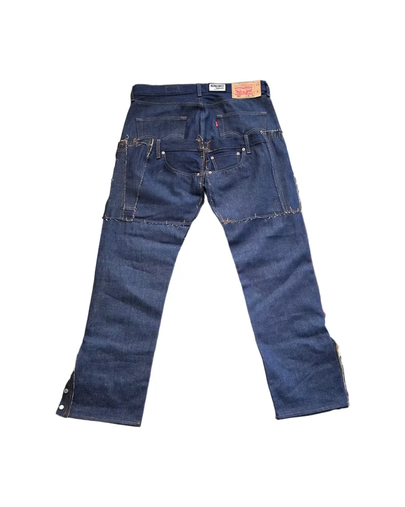 Back view of RCNSTRCT Studio Raw Denim Multi Pocket Pant featuring dark indigo denim, reinforced patchwork panels, layered utility pockets, and visible contrast stitching detailing