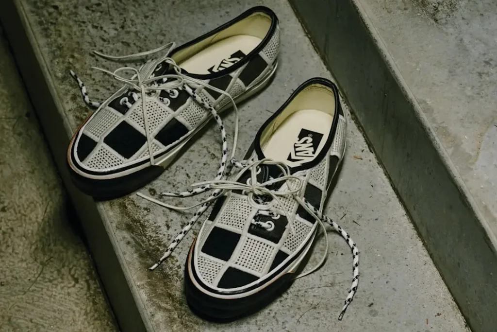 Pair of black-and-white checkerboard Vans Authentic sneakers with breathable mesh panels and rope laces placed on concrete steps, highlighting the classic skate silhouette from Vans