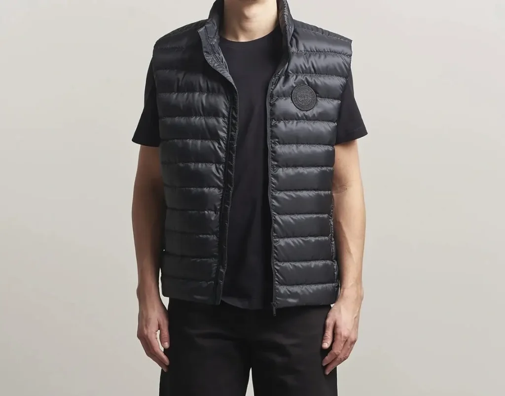 Front view of a model wearing the Canada Goose Men’s Stratus Vest in black (SKU 2490MT-9061), featuring lightweight quilted insulation, stand collar, full-zip closure, and tonal Canada Goose chest logo patch layered over a black T-shirt