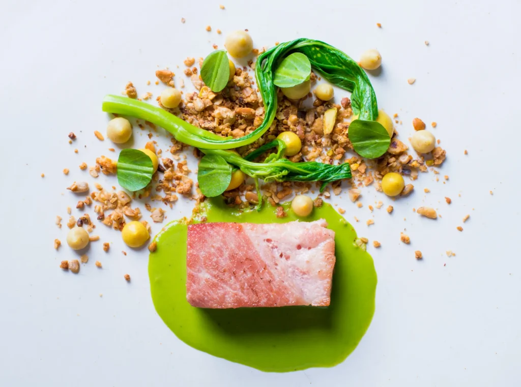 Plated fine dining dish at The SEASONS featuring a seared fish fillet on vibrant green herb sauce, accented with leafy greens, crisp textures, and delicate garnishes arranged in a minimalist composition