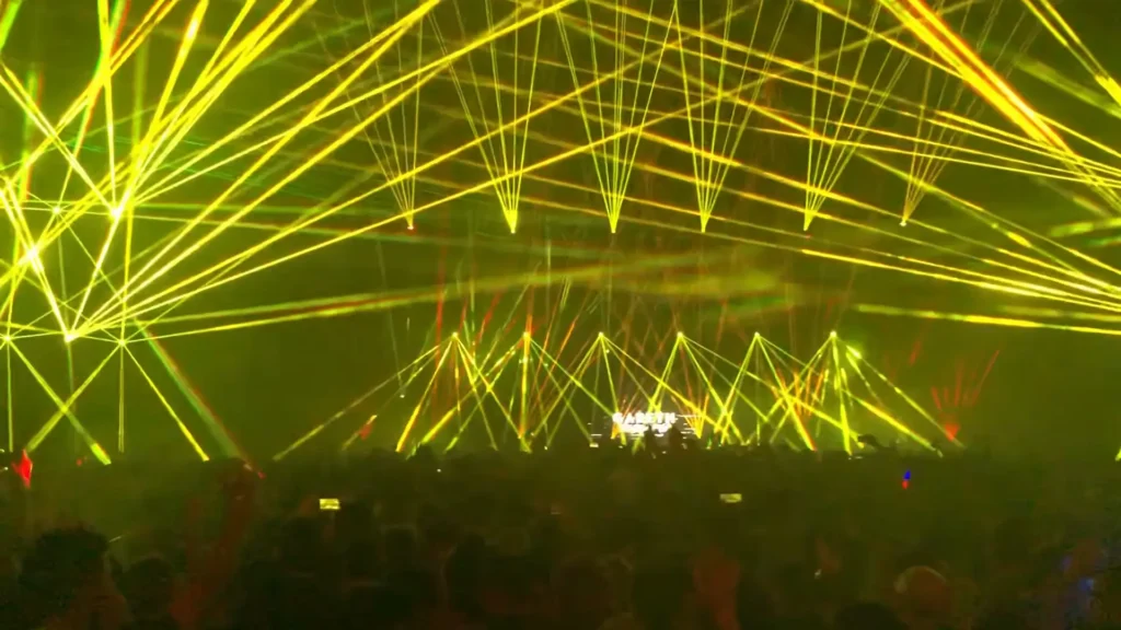Crowd dancing under bright stage lights and falling confetti during a packed electronic music party at a nightclub