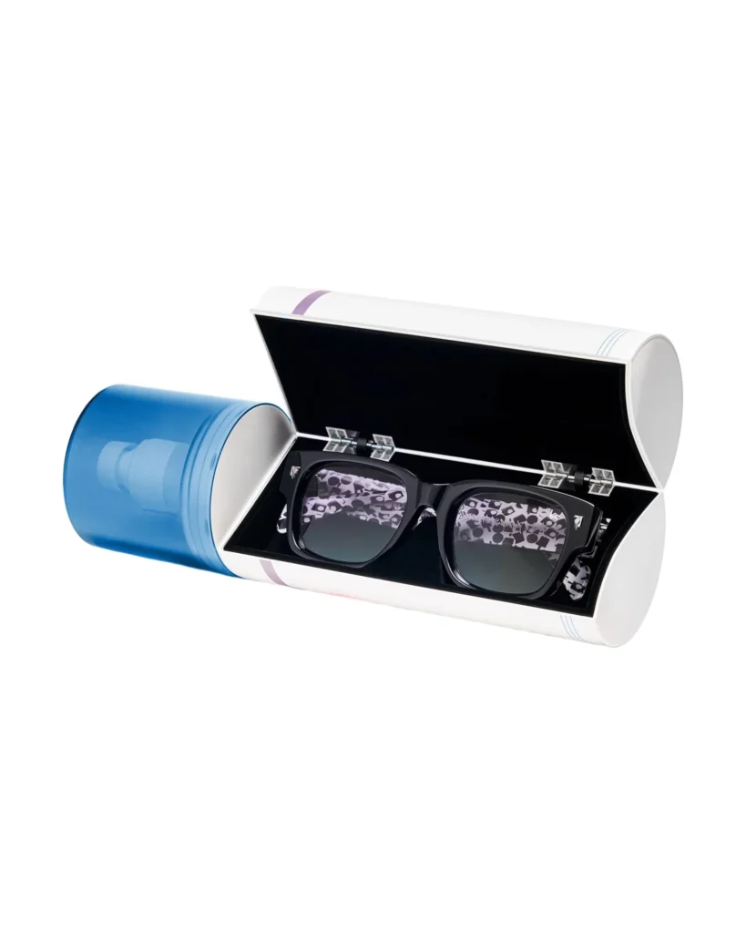 Vintage Frames Company Bowie Limited Edition sunglasses resting inside an open cylindrical presentation case with blue exterior, black interior lining, and patterned lenses reflecting the Stash Trilogy design
