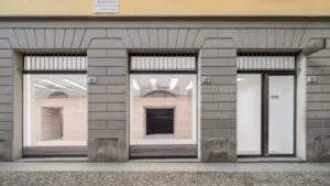 Street view of the Blumarine boutique façade at Via Fiori Chiari 28 in the Brera District, featuring large storefront windows that reveal the minimalist travertine interior designed by NM3 Studio