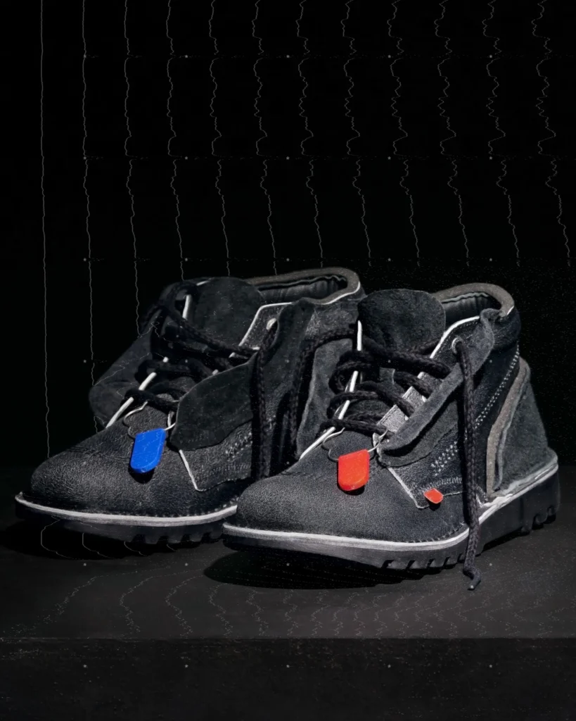 Black suede Kickers x A-COLD-WALL* limited-edition silhouette featuring rugged lug sole, exposed stitching, padded collar, and signature red and blue lace tabs against a dark minimalist backdrop