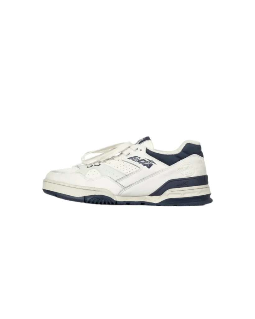 Side profile of the Chemist Creations AVIA 855 sneaker featuring cream leather upper, navy heel panel, AVIA logo branding, perforated midfoot panels, and vintage-inspired running sole