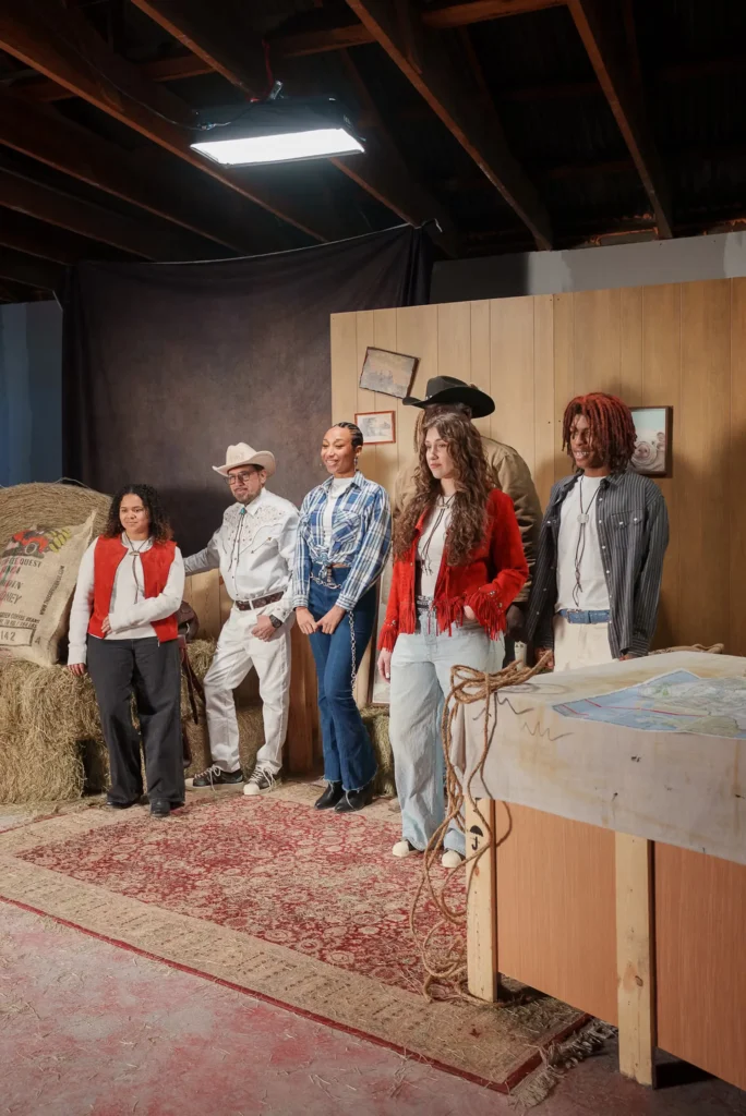 Group of models in Western-inspired outfits posing on a ranch-style set with hay bales and cowboy hats for the Adidas adidas Superstar “Lone Star Reppin’” campaign