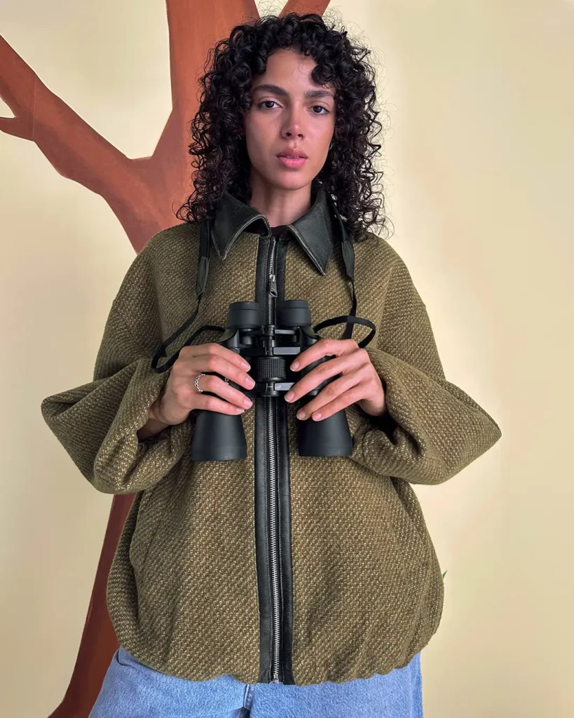 Model holding binoculars wearing textured jacket in Axel Arigato Akaia campaign with Reggieknow