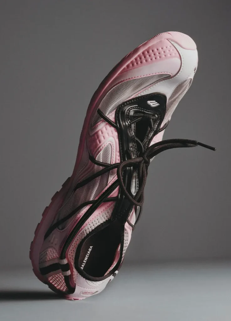 Balenciaga Radar Shoe in soft pink and white with contrasting black lacing system, shown in a dynamic suspended pose; features breathable mesh panels, sculpted overlays with subtle debossed detailing, and a streamlined low-profile sole, emphasizing the shoe’s lightweight construction, flexibility, and balletcore-inspired design direction
