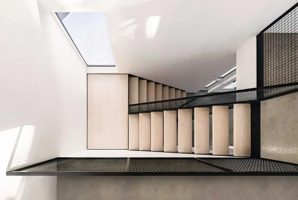 Overhead view of the modern staircase inside the Columbia River Valley Lookout cabin by Twobytwo Architecture featuring light wood steps, black steel mesh flooring, and a skylight illuminating the minimalist interior