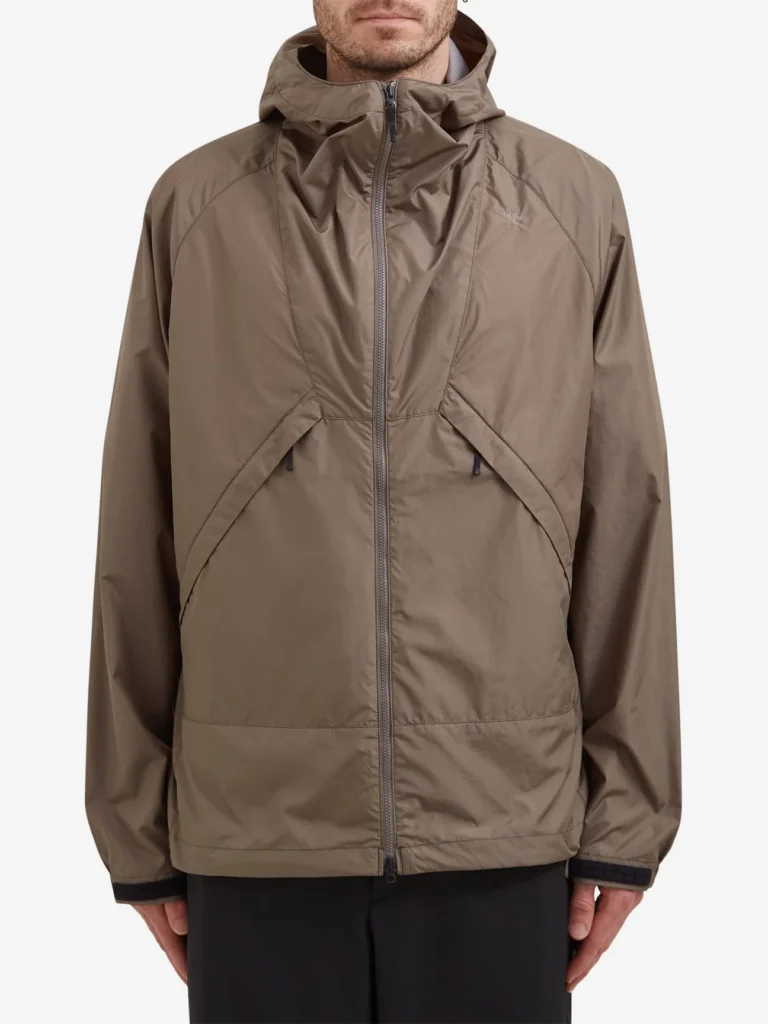 Model wearing the Goldwin Rip Stop Hooded Jacket in olive, a lightweight technical outerwear piece with ripstop fabric, structured hood, front zip closure, and minimalist outdoor design