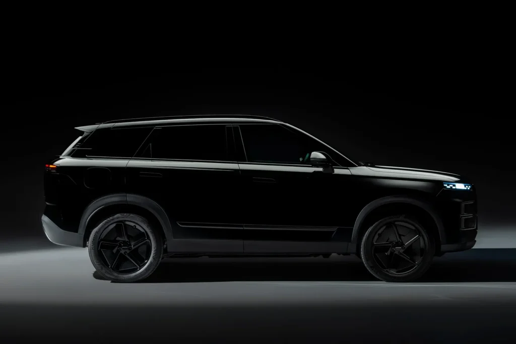 Side profile of the Jaecoo 7 SUV in a dark studio setting, finished in black with a clean, boxy silhouette, slim LED lighting accents, tinted windows, and large multi-spoke alloy wheels