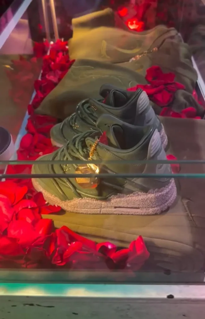 Teyana Taylor x Air Jordan 3 SP “Concrete Rose” sneaker displayed in a glass case with deep green leather upper, cement-textured midsole, gold rose charm on the laces, and red rose petals surrounding the shoe