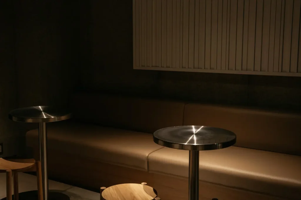 Minimalist seating area inside PASS listening bar featuring leather bench seating, round metal tables, and acoustic wall panels