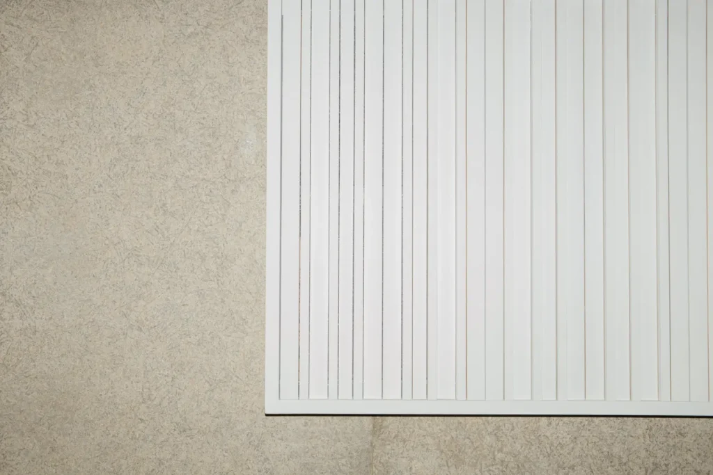 Close-up of architectural acoustic panels with white vertical slats installed on a textured stone wall, illustrating minimalist interior sound design used in listening bars and audiophile spaces