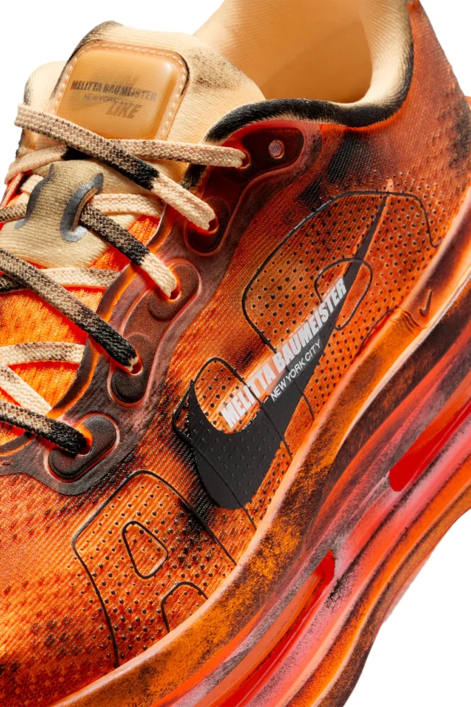 Close-up detail of the Melitta Baumeister x Nike Vomero Premium in Total Orange, highlighting distressed mesh, charred overlays, co-branded Swoosh with “Melitta Baumeister New York City” text, and textured sculptural midsole