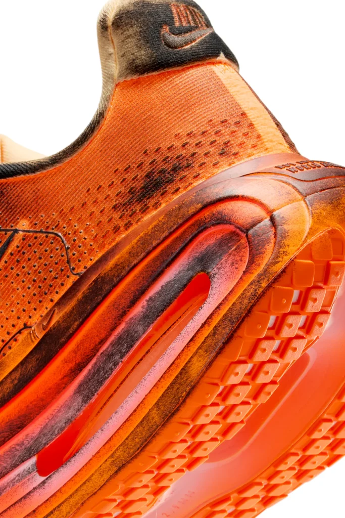 Close-up of the heel and midsole on the Melitta Baumeister x Nike Vomero Premium in Total Orange, showing charred distress detailing, textured mesh upper, and the sculpted Air unit with visible cushioning