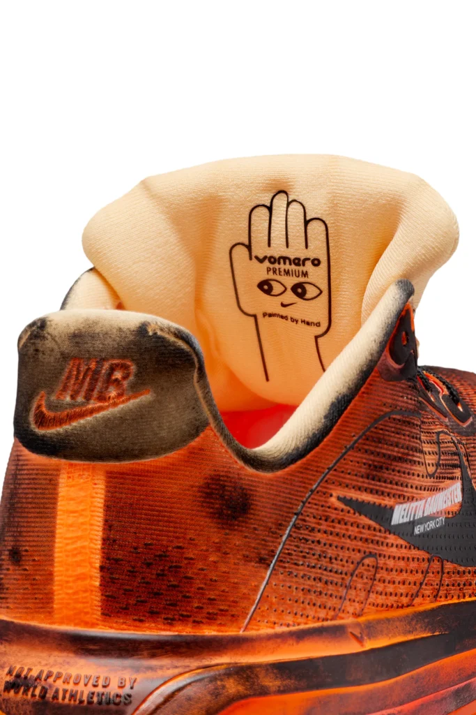 Close-up of the heel collar and tongue on the Melitta Baumeister x Nike Vomero Premium in Total Orange, featuring distressed lining, Nike Air embroidery, and inner tongue graphic reading “Vomero Premium – Painted by Hand” with illustrated hand and eye motif