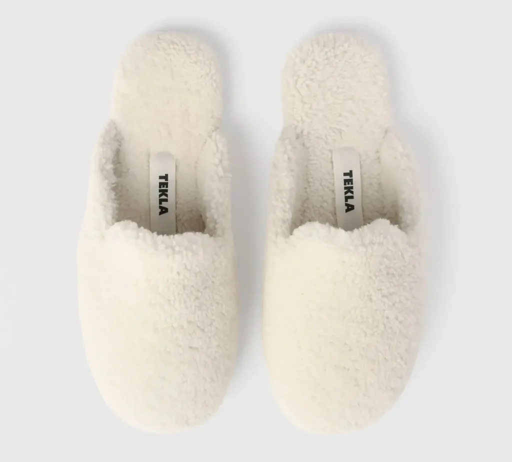 Top-down view of cream shearling Tekla slippers, featuring plush wool texture, rounded toe shape, and interior labels with minimalist Tekla branding