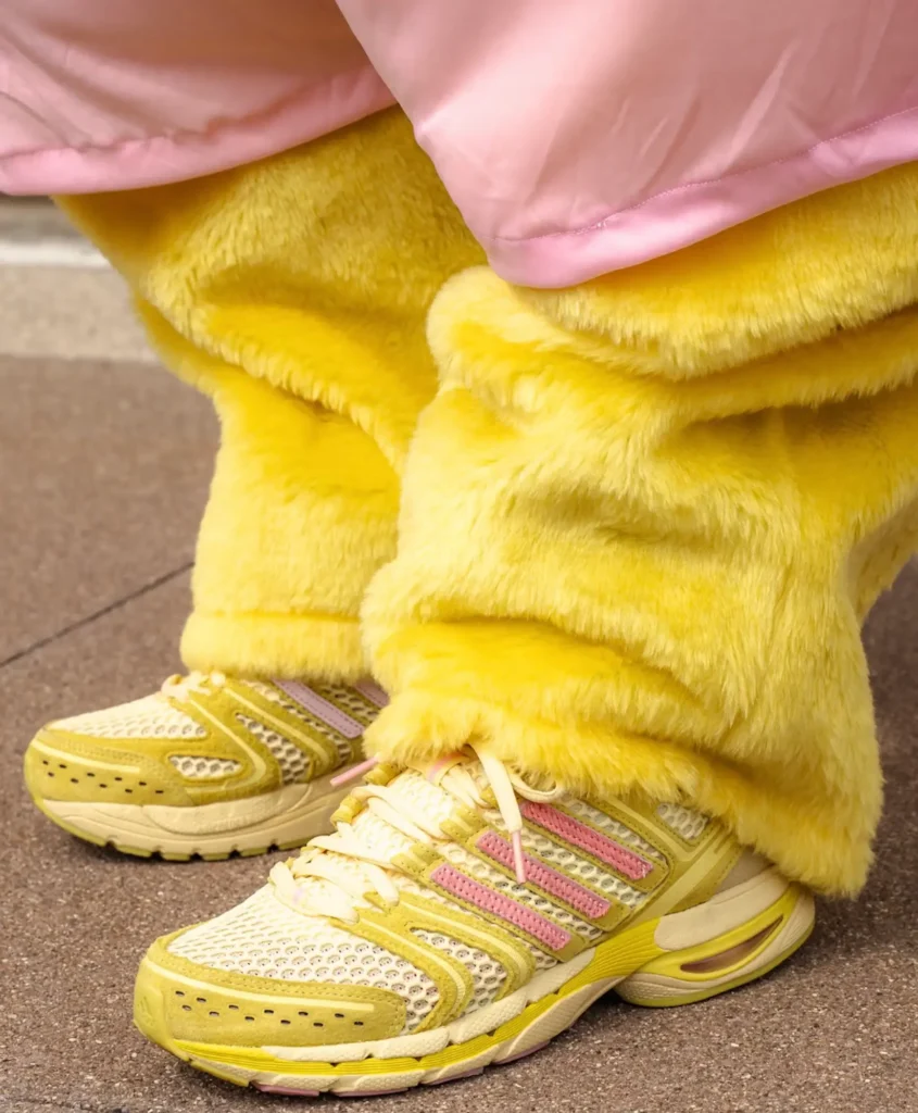 Close-up of yellow and pink mesh running sneakers with suede overlays, styled with oversized fuzzy yellow pants and a pink jacket, highlighting playful textures and vibrant color blocking