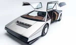 Futuristic wedge-shaped Aston Martin concept car with sharp angular bodywork, gullwing-style doors open, and minimalist interior displayed against a clean white studio background