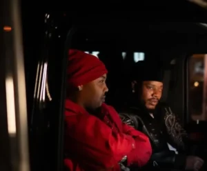 left G hero as right side Fetty Wap inside a dimly lit vehicle at night, one in a red headwrap and matching jacket, the other in a black cap and leather jacket, both facing forward in a reflective, subdued moment that mirrors the introspective tone of the song