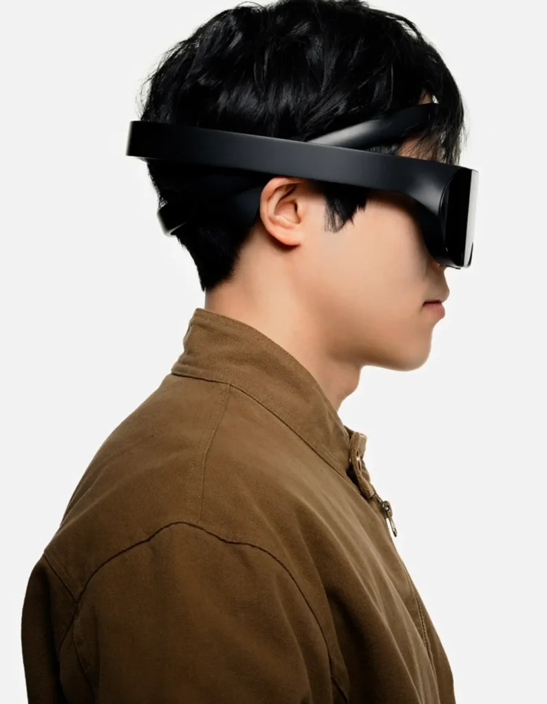 Side profile of a person wearing a sleek, matte-black neuro-responsive headset with a continuous wraparound band and visor, designed with minimal form to integrate EEG sensing and adaptive augmented reality visuals