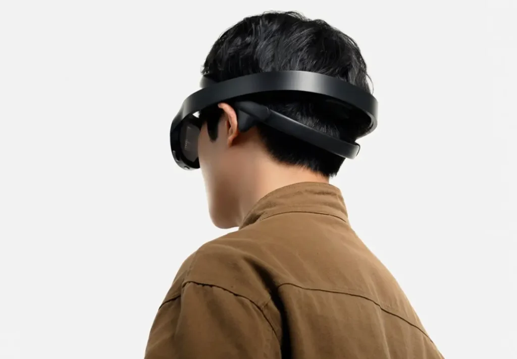 Rear three-quarter view of a person wearing a minimalist black neuro-responsive headset with a dual-loop band wrapping around the head, highlighting its integrated EEG sensor placement and seamless augmented reality design