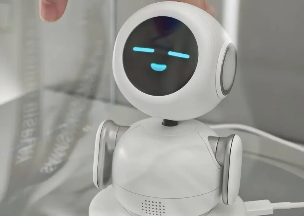 Samsung Mini PetBot AI robot with circular OLED face displaying relaxed blue eyes while a hand gently taps the top of the small white companion robot