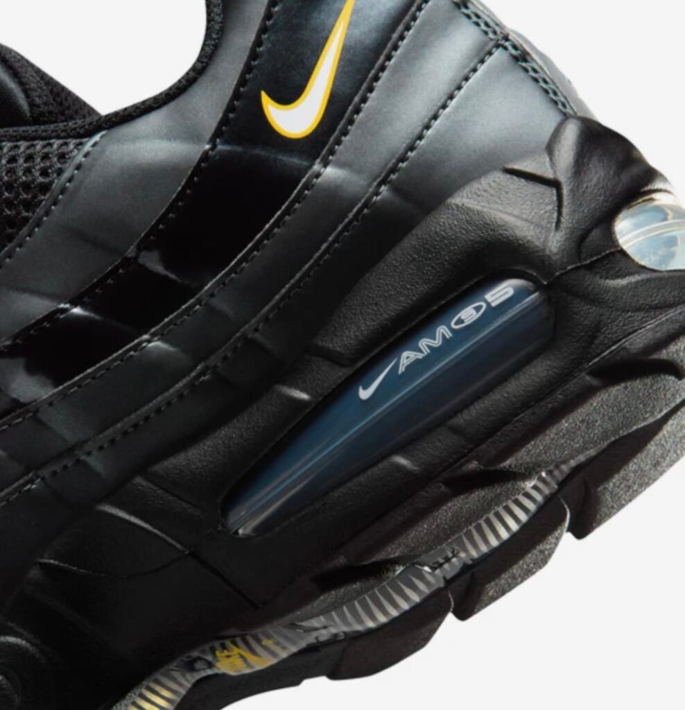 Close-up detail of the Nike Air Max 95 “Black / White – University Gold” showing glossy layered side panels, gold mini Swoosh, and visible Air Max heel cushioning unit