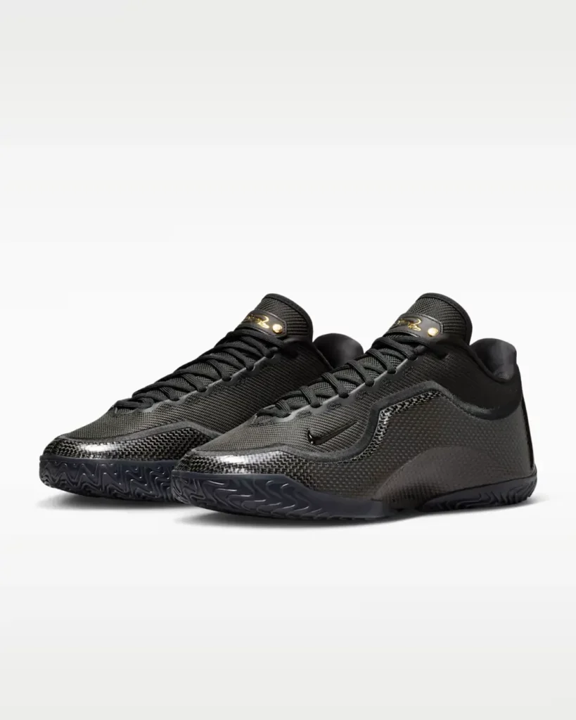 Pair of Nike LeBron XXIII “Masked Menace” basketball shoes in black, shown in angled front view with textured woven uppers, carbon-fiber-style side panels, gold signature tongue details, and low-profile performance build