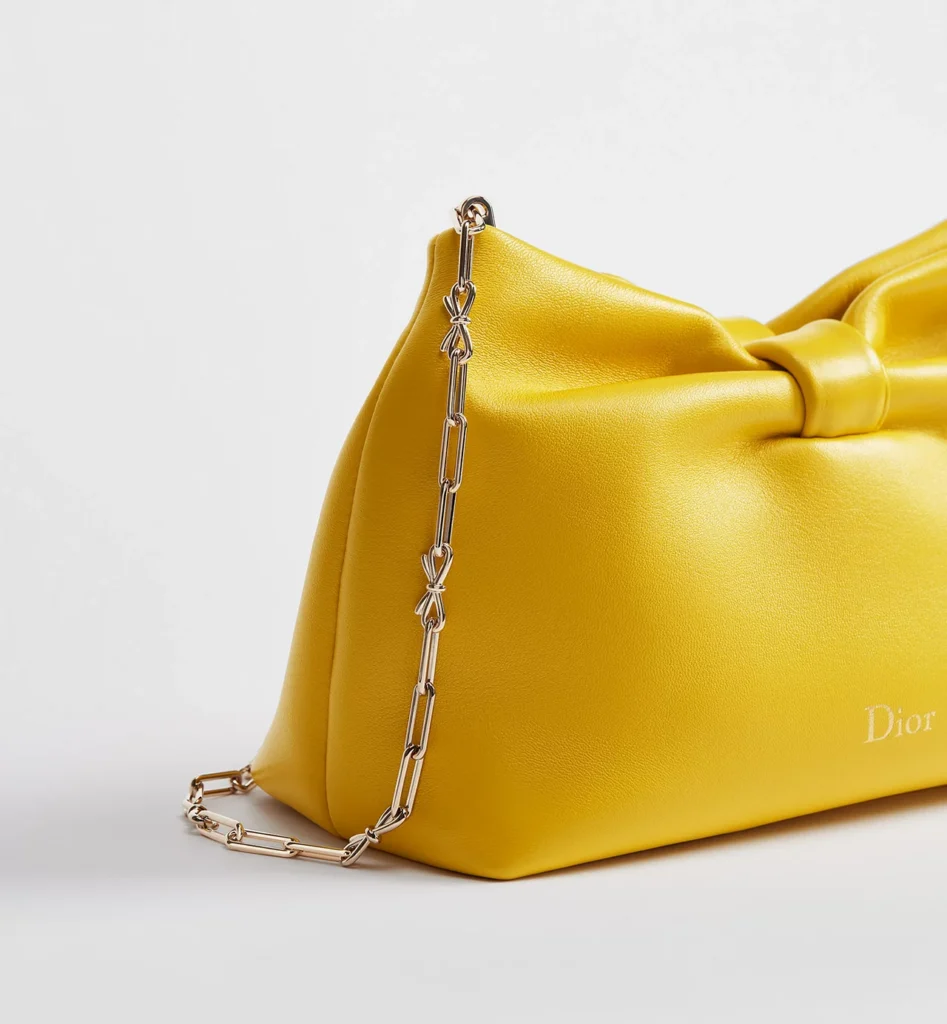 Side view of the Small Dior Bow Bag in buttercup yellow lambskin featuring sculpted bow detailing and a gold-tone chain strap with delicate bow-shaped hardware accents