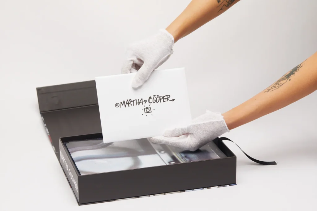Hands wearing white gloves holding a signed card by Martha Cooper from the Spray Nation limited edition graffiti photography box set
