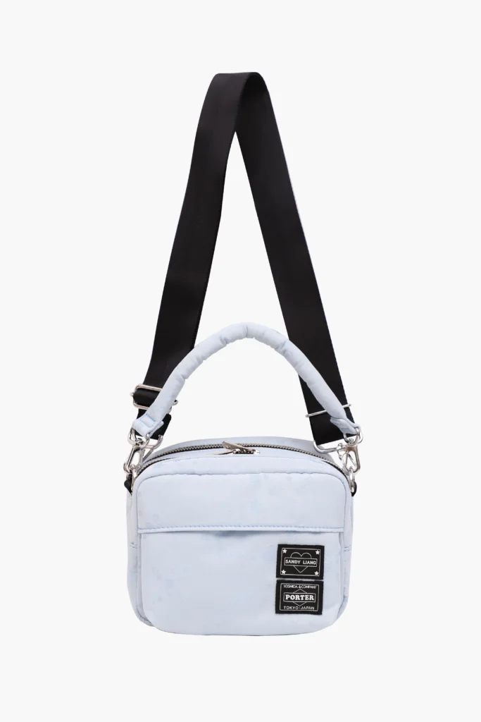 Light blue Andy Liang x Porter Muffin Bag with padded top handle and detachable black shoulder strap, featuring subtle star and heart motifs and co-branded Sandy Liang and Porter patches on the front