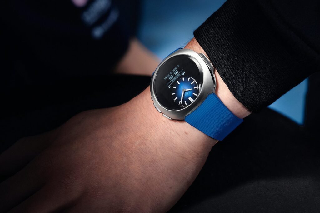 Wrist shot of the H. Moser Streamliner Alpine Mechanics Edition with a blue rubber strap, showing a hybrid analog-digital display on a curved black screen