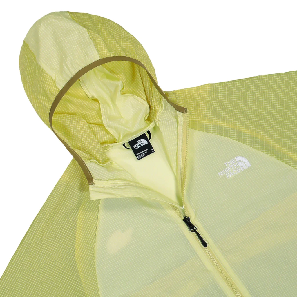 Close-up of The North Face NSE Wind Jacket in Lemon Mist and Pear, highlighting the adjustable hood, ripstop grid fabric, front zip closure, and subtle white logo on the chest