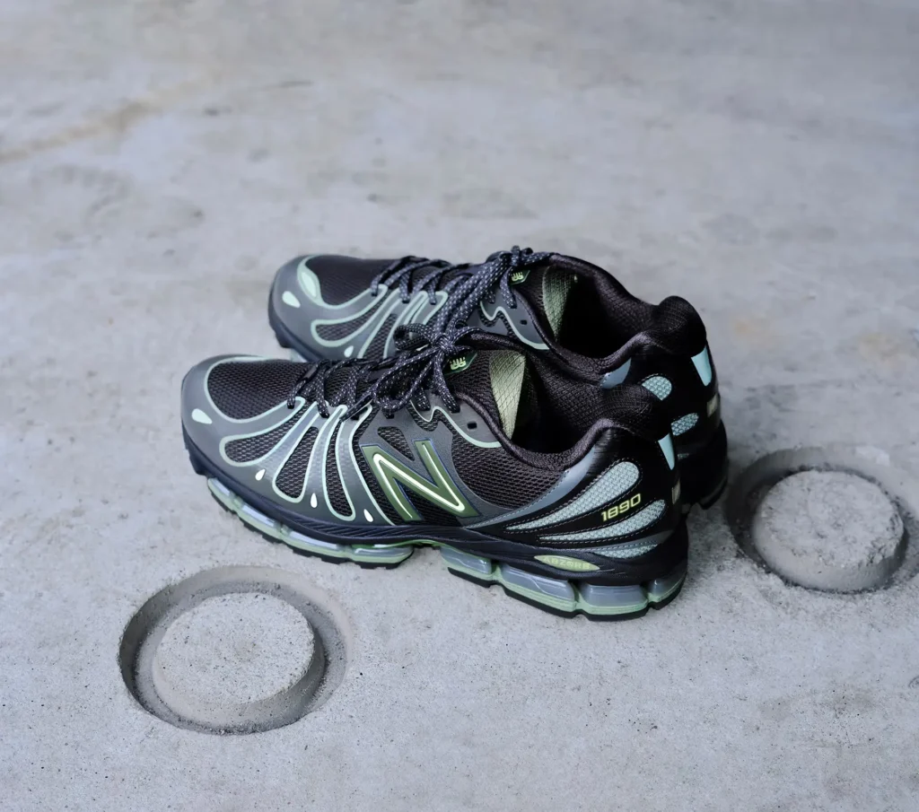 Pair of black and olive-accented New Balance 1890 sneakers placed on a concrete floor, highlighting the breathable mesh upper, flowing synthetic overlays, and segmented ABZORB cushioning midsole