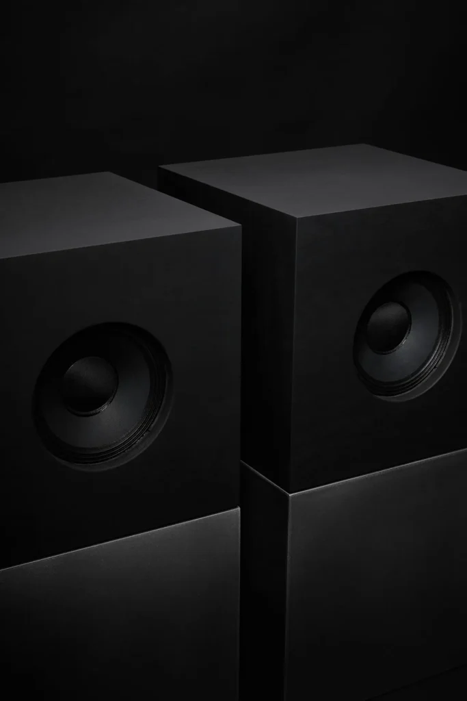 Minimalist cubist-inspired stereo speakers by Nocs and industrial designer Daniel Alm, featuring stacked black and brushed-metal cube enclosures with circular drivers, photographed against a dark background