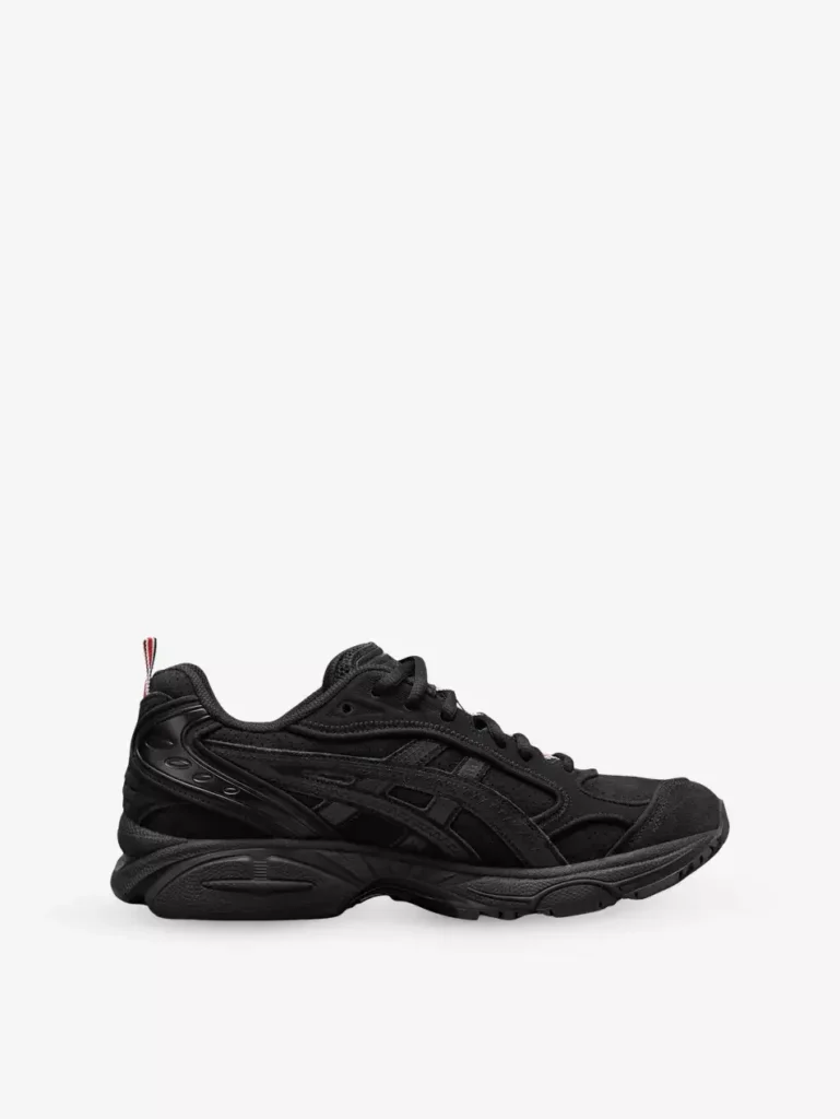 Side profile of Thom Browne x ASICS GEL-Kayano 14 woven trainers in all-black, featuring textured woven upper, tonal ASICS overlays, sculpted midsole with GEL cushioning, and signature red, white, and blue heel tab detail.