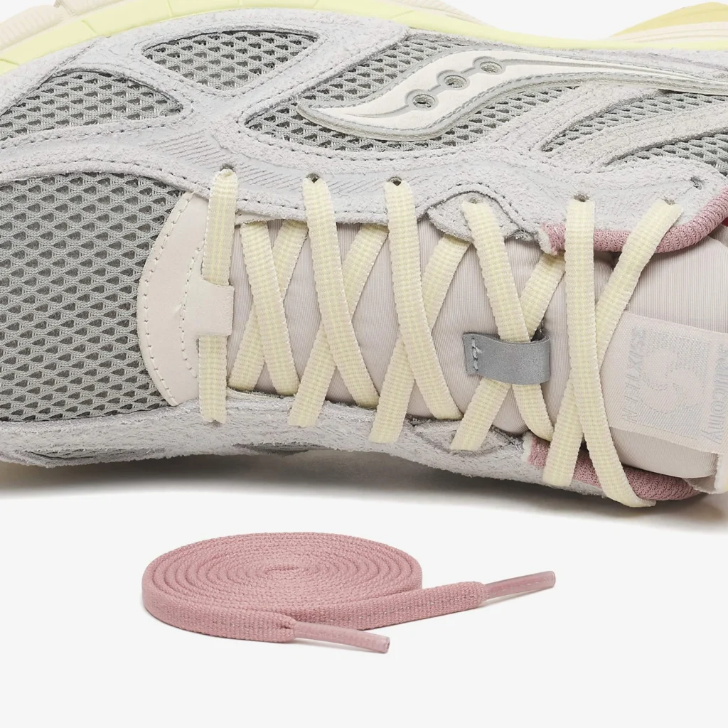 Close-up detail of Saucony x 3sixteen Guide 7 “Graphite” showing grey mesh and suede upper, cream lacing system with reflective loop, and included pink spare laces displayed below