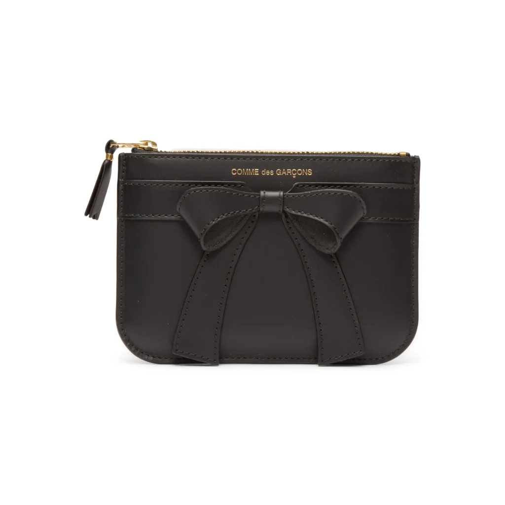 Black leather Comme des Garçons Big Bow pouch with stitched bow detail on the front, gold COMME des GARÇONS logo and gold zip closure