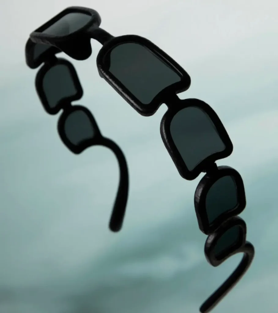 Issey Miyake Eyes UROKO sunglasses floating against a soft gradient background, featuring eight concave dark-tinted lenses arranged in a segmented row within a sculptural black 3D-printed frame inspired by Shoji Kamoda’s ceramic scale patterns