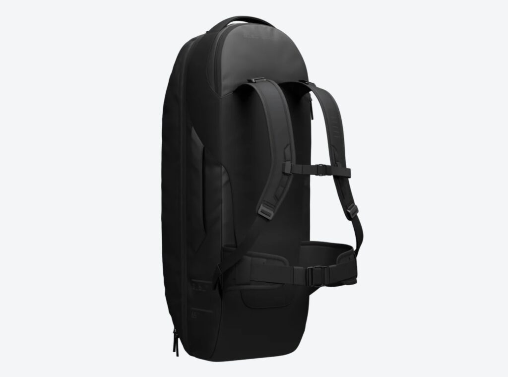 Side view of the Db Journey Skate Duffel 65L showing the structured black shell, ergonomic backpack straps, and supportive waist belt designed for comfortable carrying during travel