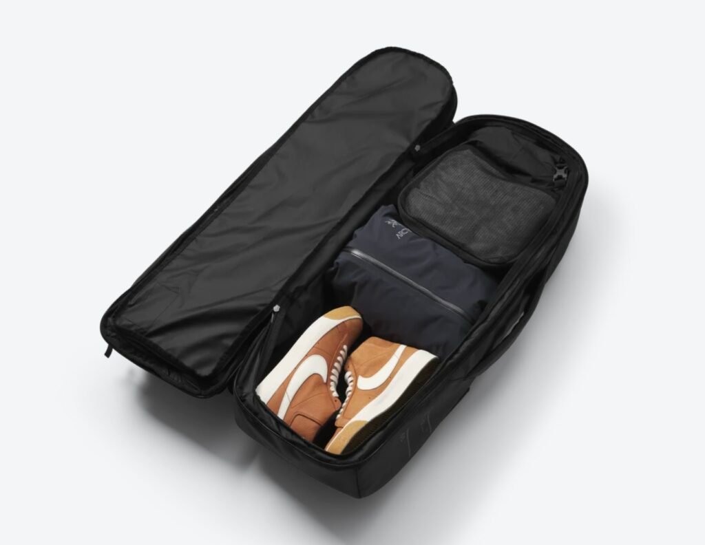 Main clothing compartment of the Db Journey Skate Duffel 65L opened to show packed travel items including sneakers, a jacket, and organized storage pouches